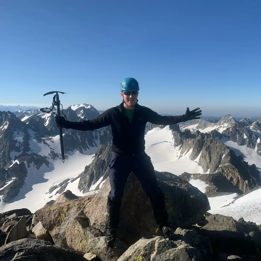 William Loopesko at the top of a mountain with his hands raised